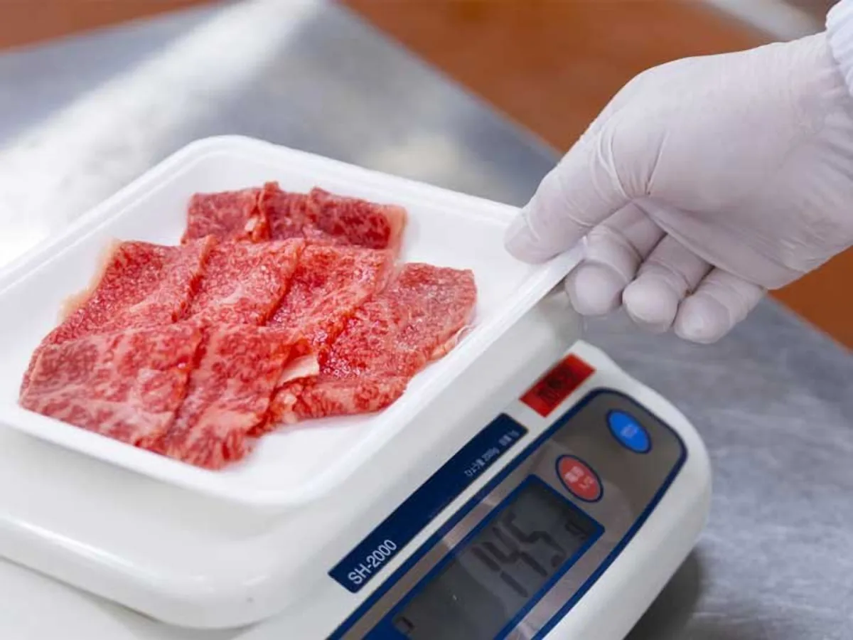 手袋をした手で、スライスした牛肉をはかりにのせる