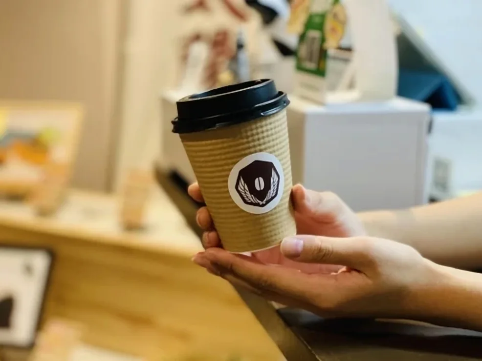 ロゴ入りのカップで手渡すテイクアウトのコーヒー