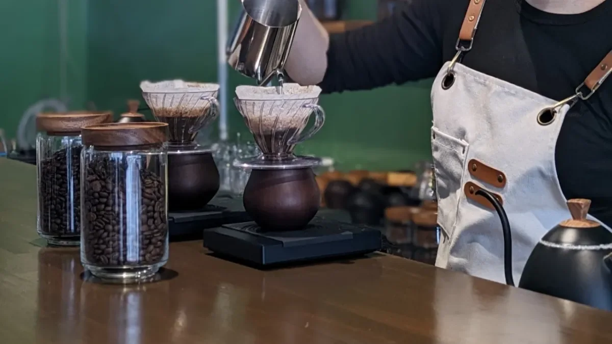 カウンターで一杯ずつハンドドリップするバリスタの手元と、瓶に入ったコーヒー豆