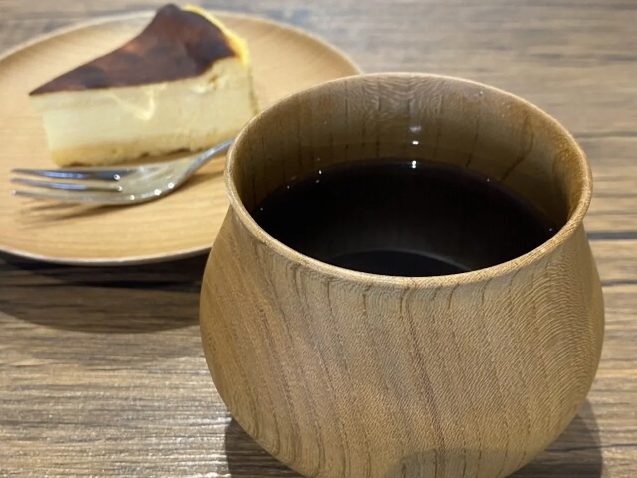 木のカップに注いだコーヒーと、バスクチーズケーキの一切れ