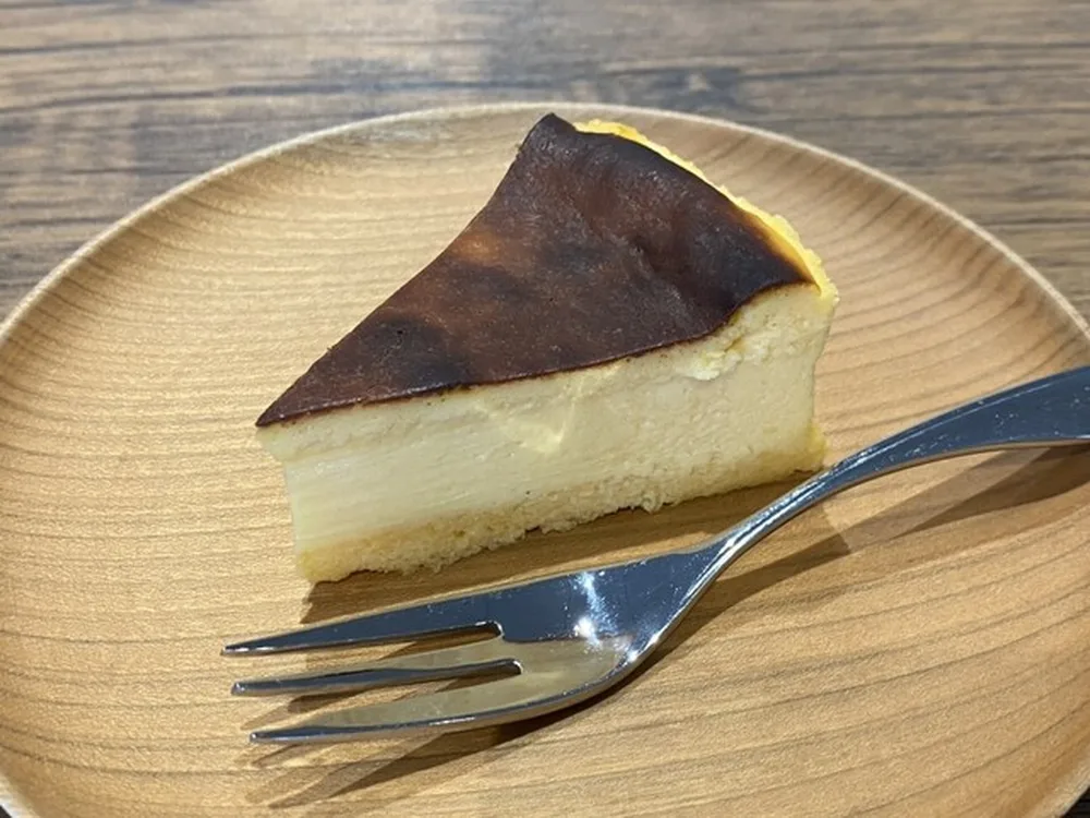 木の皿にのせた、表面を焼き上げたチーズケーキの一切れ