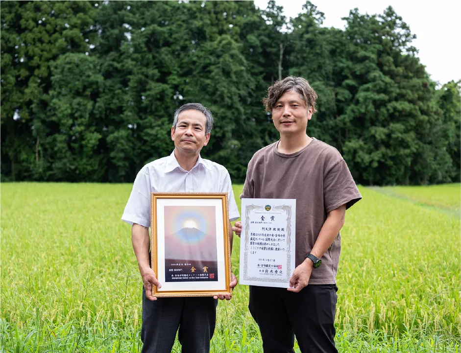 賞状を手に田んぼの前に立つ阿久津政英さん