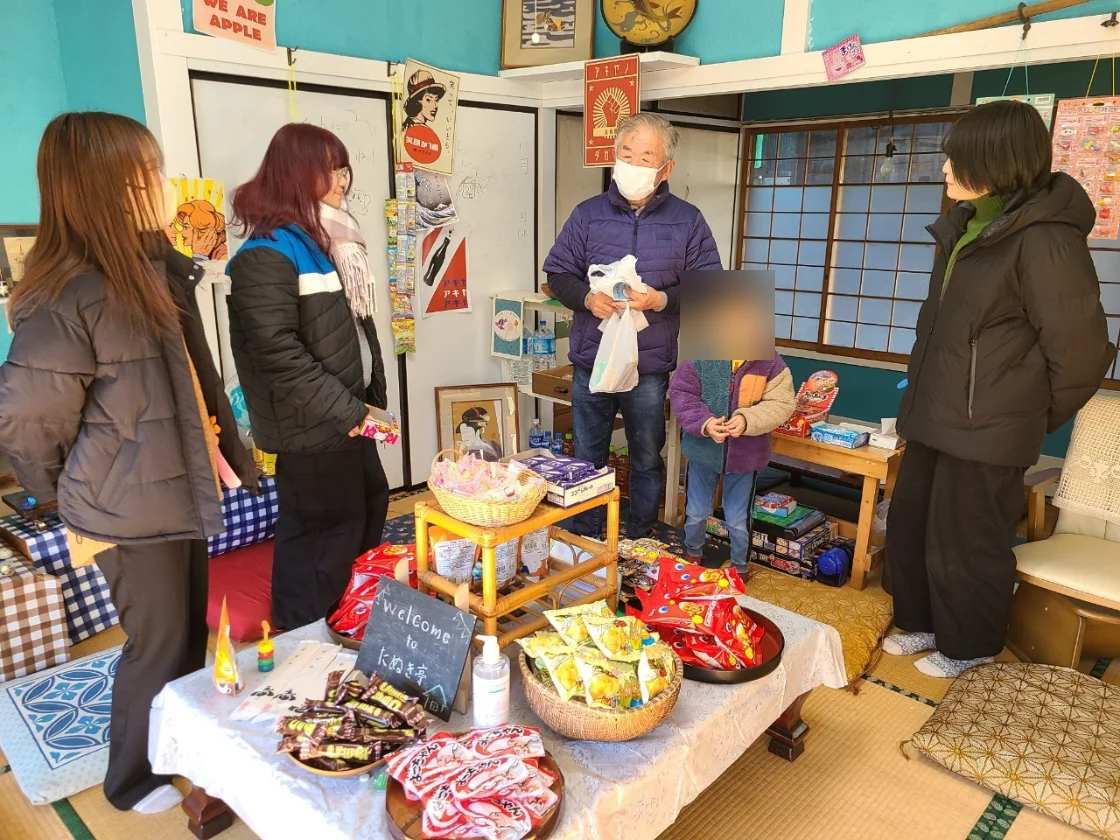 駄菓子を並べたテーブルを囲み、地域の人と学生が言葉を交わす和室