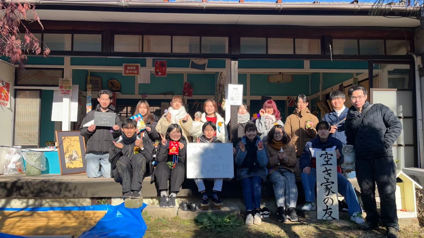 たぬき亭の縁側に並び、手づくりの看板を持つ空き家の友の学生たち