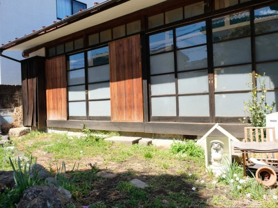 庭に置かれた、たぬきの置物が入った小さな木の小屋と縁側