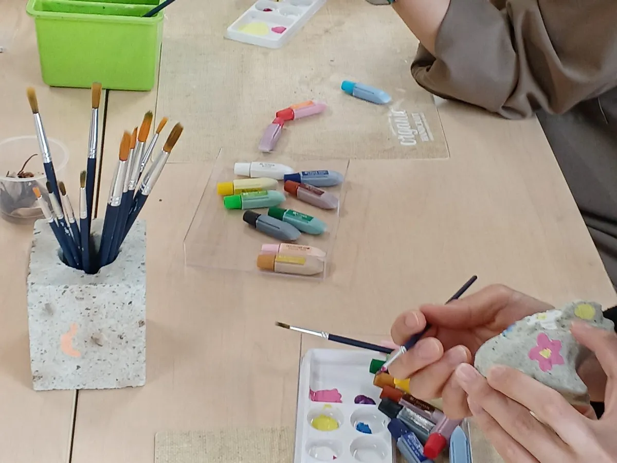 テーブルの上で、筆を使って小さな石に絵の具で色を塗る手元