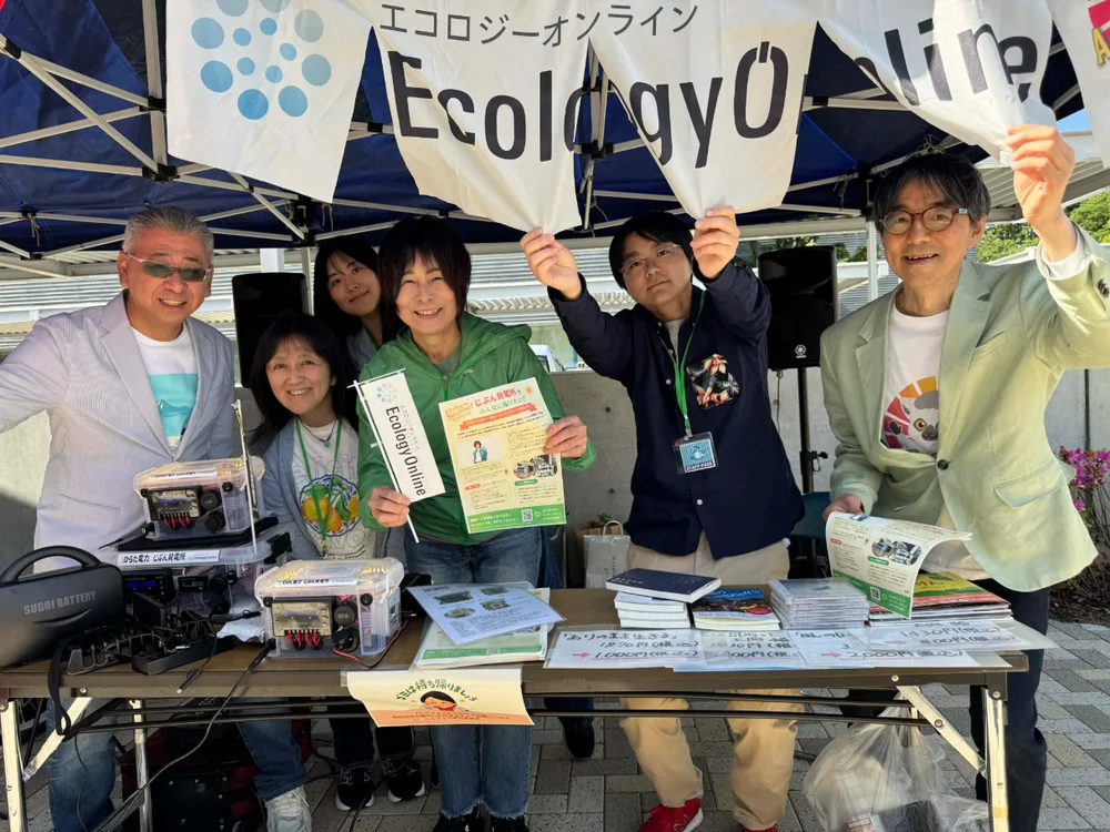 エコロジーオンラインの旗の下、発電装置や資料を並べた出展ブースに立つメンバーたち