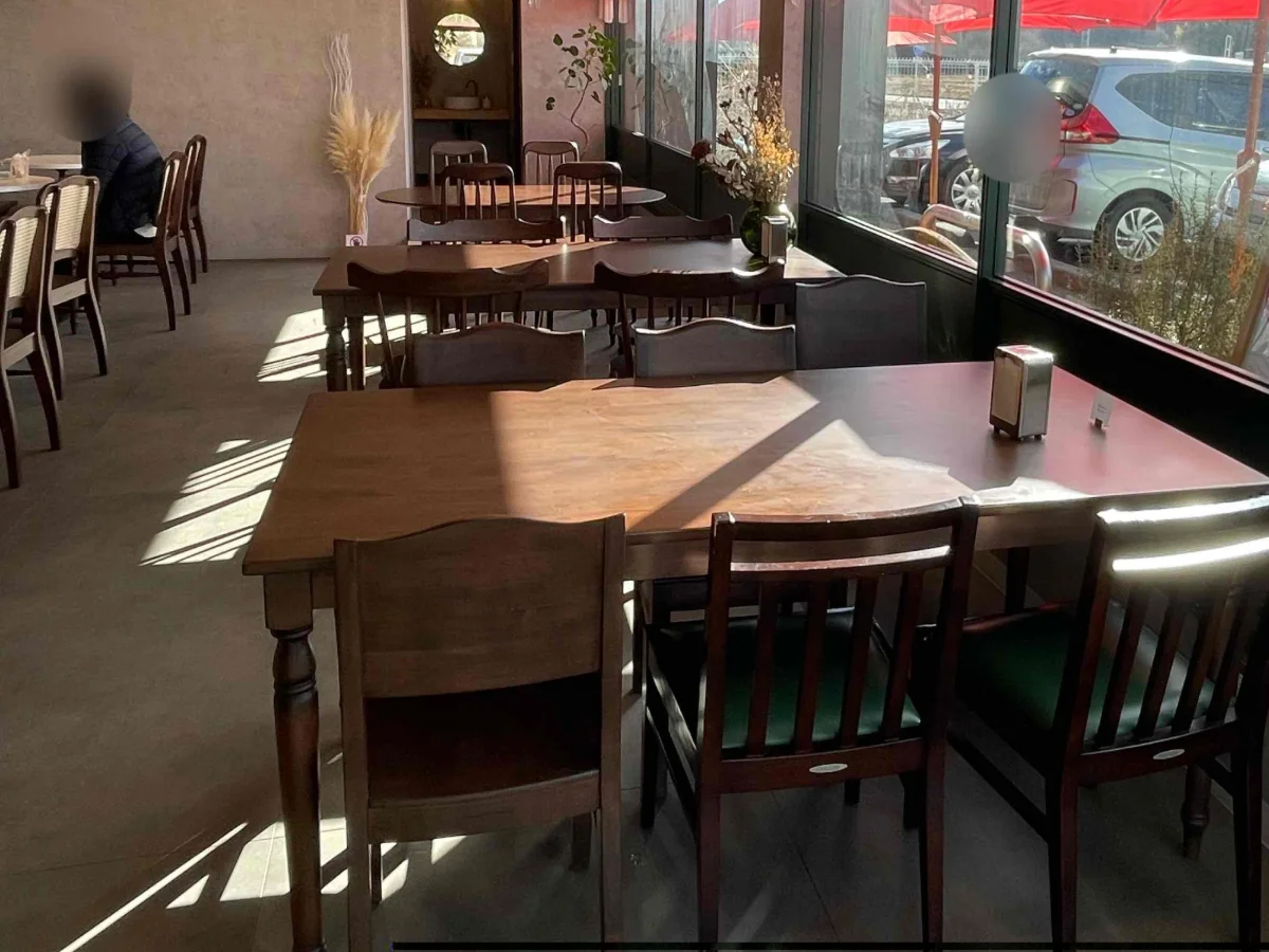 木のテーブルと椅子が並ぶ、明るいカフェの店内