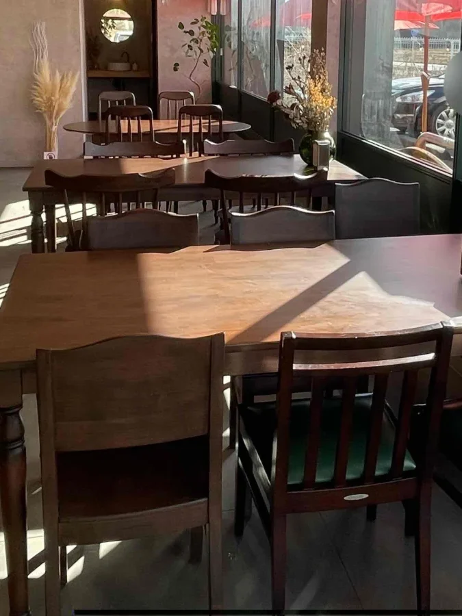 木のテーブルと椅子が並ぶ、明るいカフェの店内