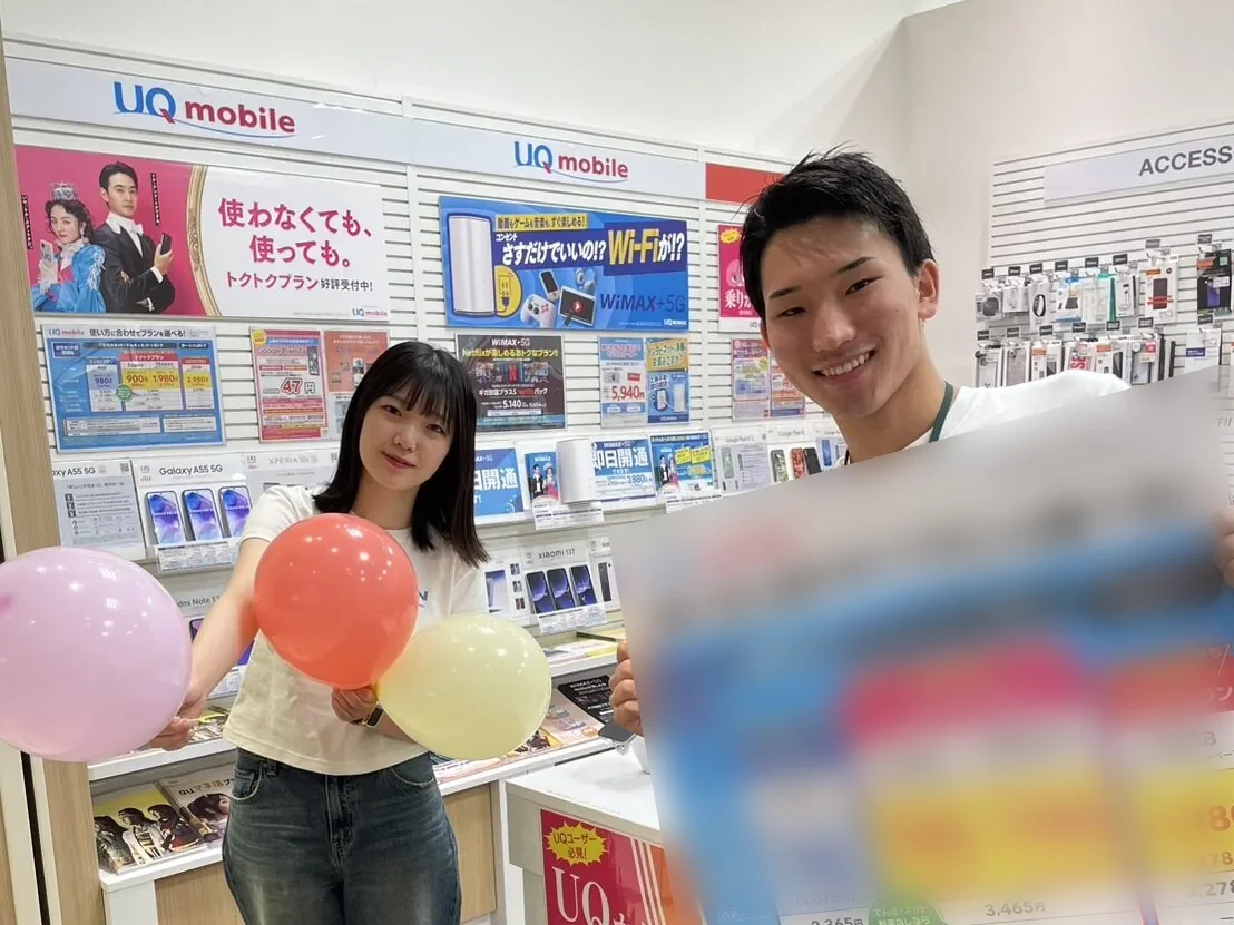 携帯ショップの売場で、料金プランの案内を手に笑顔を見せるスタッフ