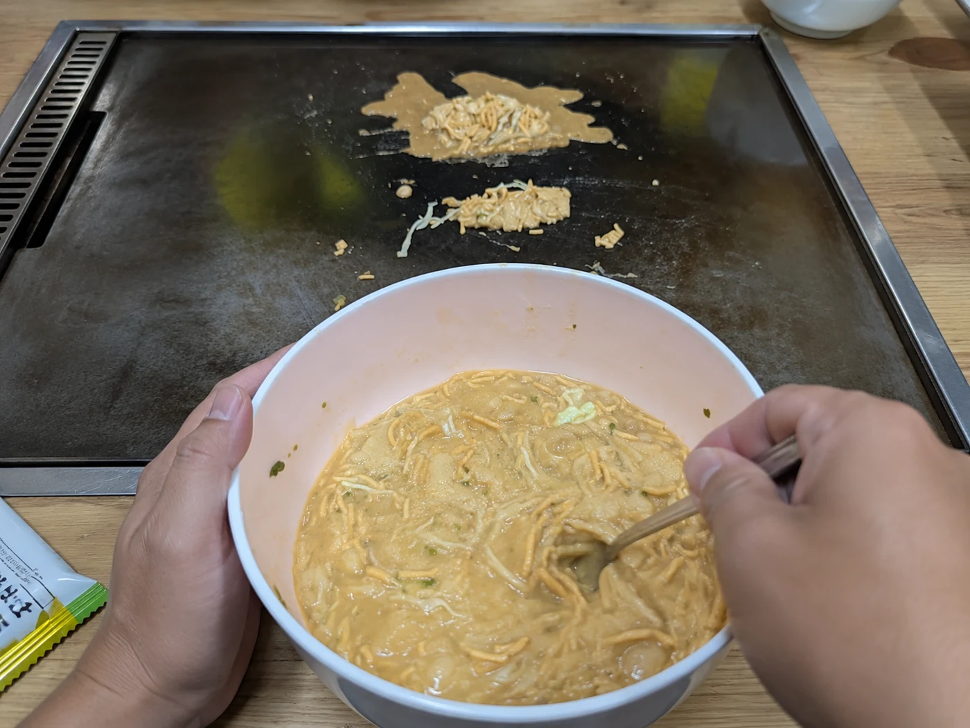 鉄板の前で、具材を混ぜた生地をボウルで混ぜる手元