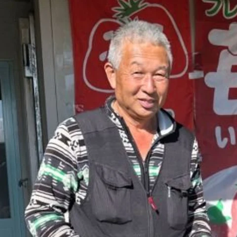 直売所の前で、いちごの箱を手にほほえむ代表の小竹哲夫さん