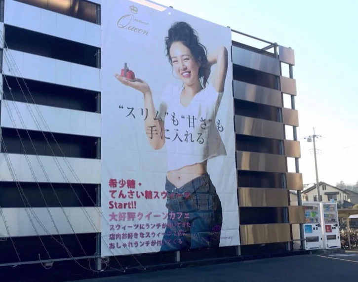 建物の壁面に掲げられた、カフェの大型広告。モデルが商品を手にほほえむ