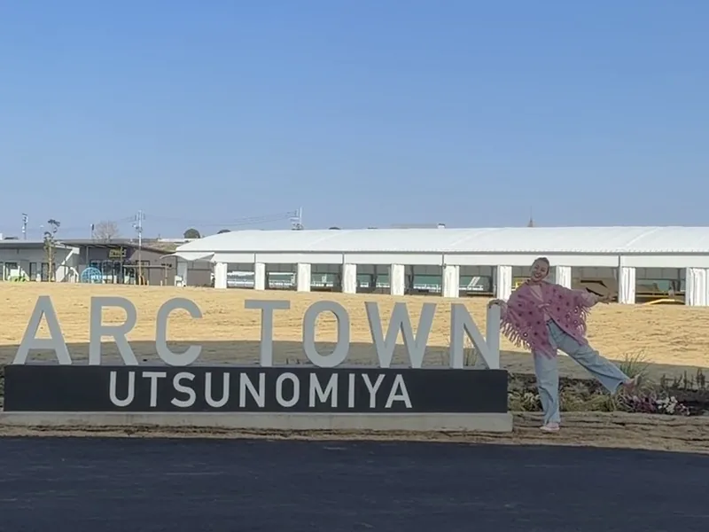 ARC TOWN UTSUNOMIYAの看板の横でポーズをとるまきえ氏