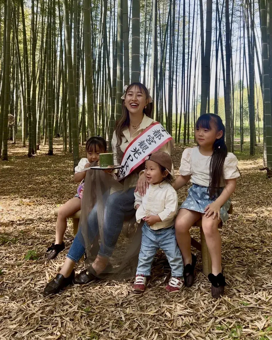 宇都宮観光PR特使のたすきを掛けたまきえ氏が、竹林で子どもたちと笑顔で座っている