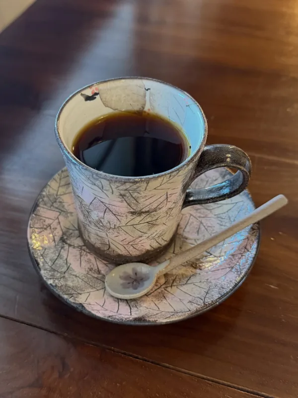 木のテーブルに置いた、葉の模様のカップとソーサーのコーヒー