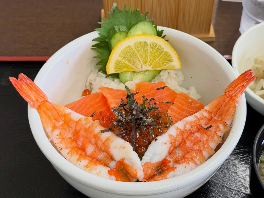 サーモンといくら、殻付きの海老を盛った丼。レモンと大葉、きゅうりが添えてある