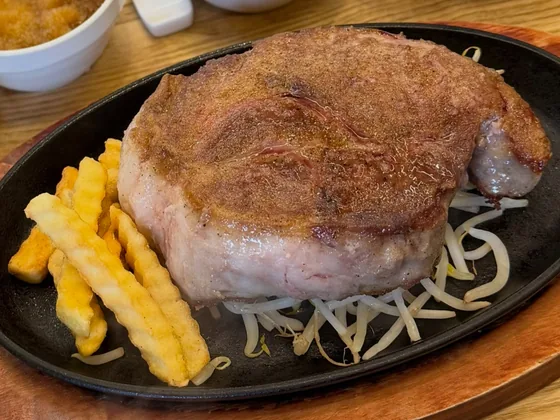 鉄板の上で焼き上がった厚切りのステーキと、フライドポテト、もやし