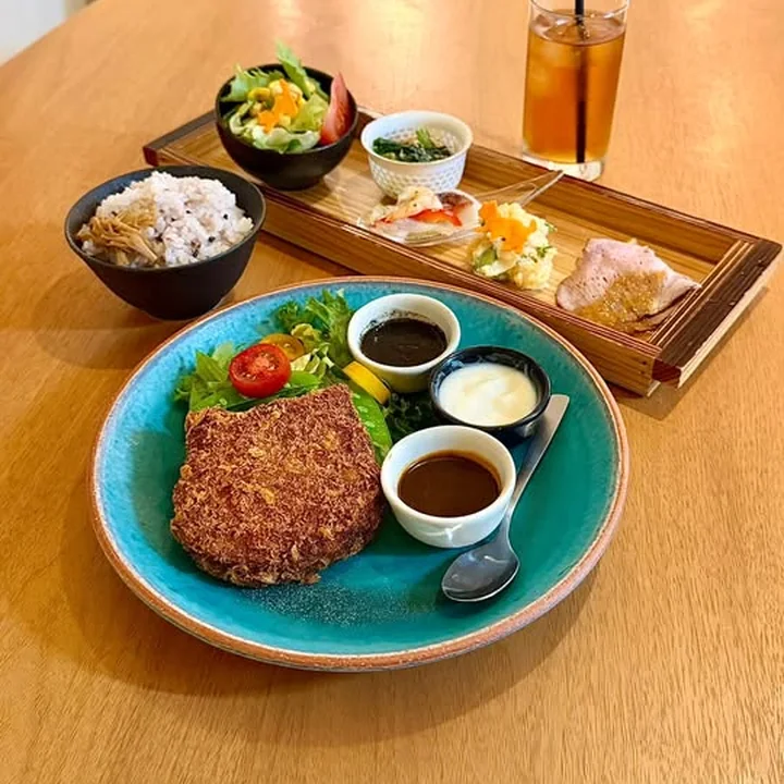 青い皿のメンチカツに、ソース3種と雑穀ごはん、小鉢を添えたコラボメニューのプレート