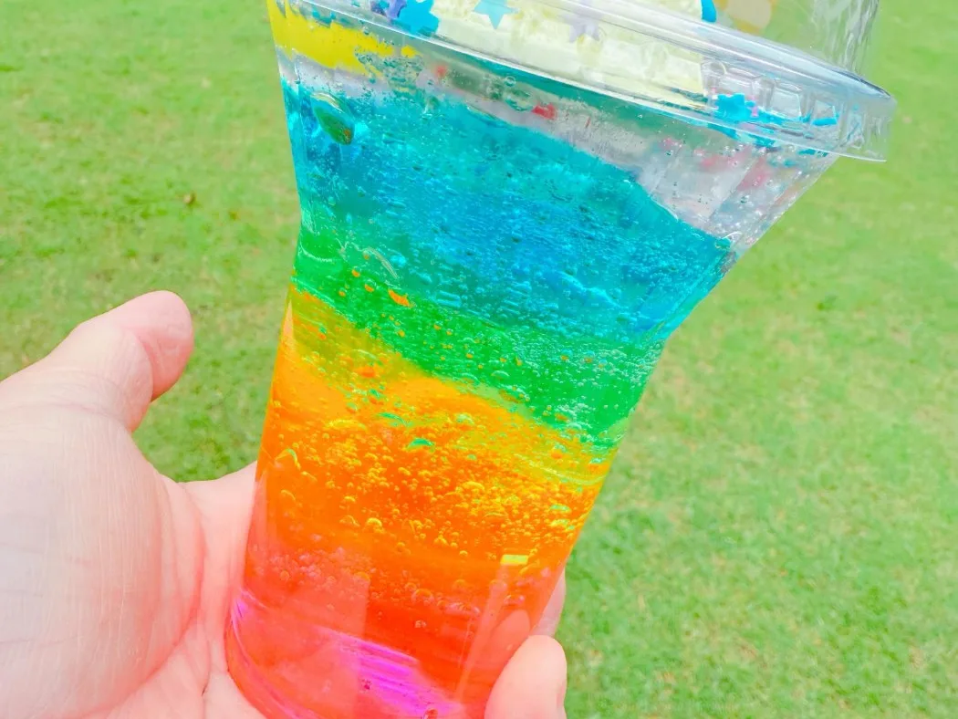 芝生を背景に、手に持った虹色のスライムパフェ