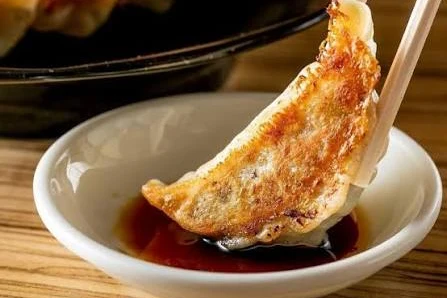 焼き目のついた餃子を箸でつまみ、小皿のたれにつける