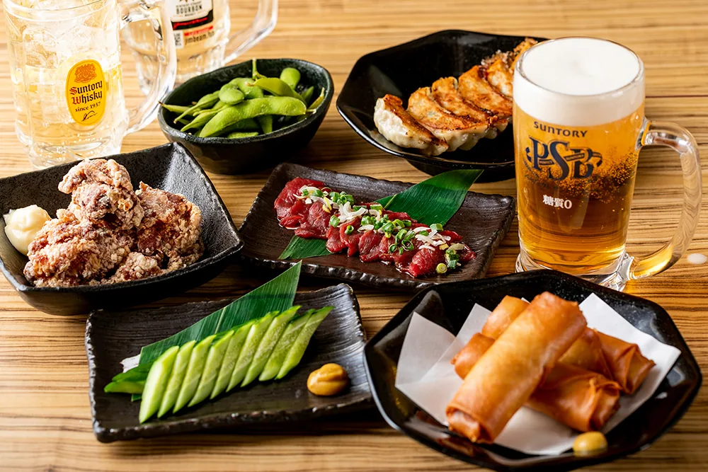 焼き餃子、唐揚げ、春巻き、馬刺しなどの料理とビールが並ぶテーブル