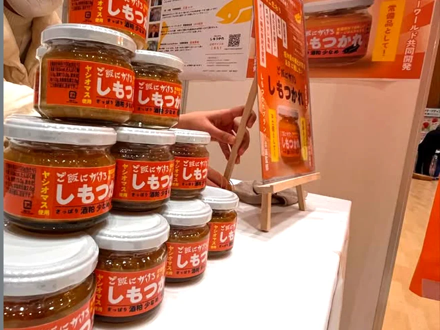 イベント会場の販売ブースに積み上げられた「ご飯にかけるしもつかれ」の瓶と紹介パネル