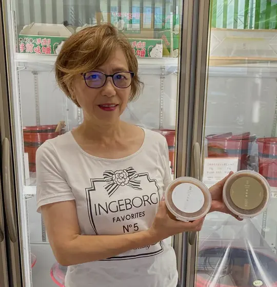 店内の冷蔵ケースの前で、大和屋の味噌を手にする代表社員の江連美智子さん