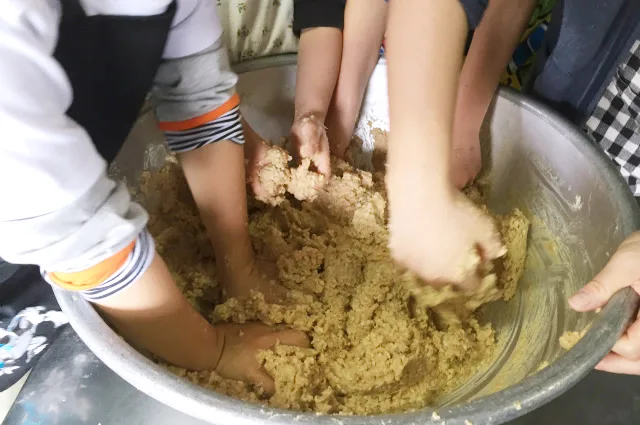 ボウルの中で、つぶした大豆と麹を手で混ぜ合わせる教室の様子