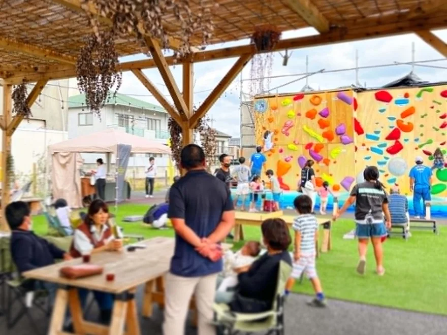 屋外の交流拠点でくつろぐ人々とボルダリングウォール。まちづくりの社会実験の風景