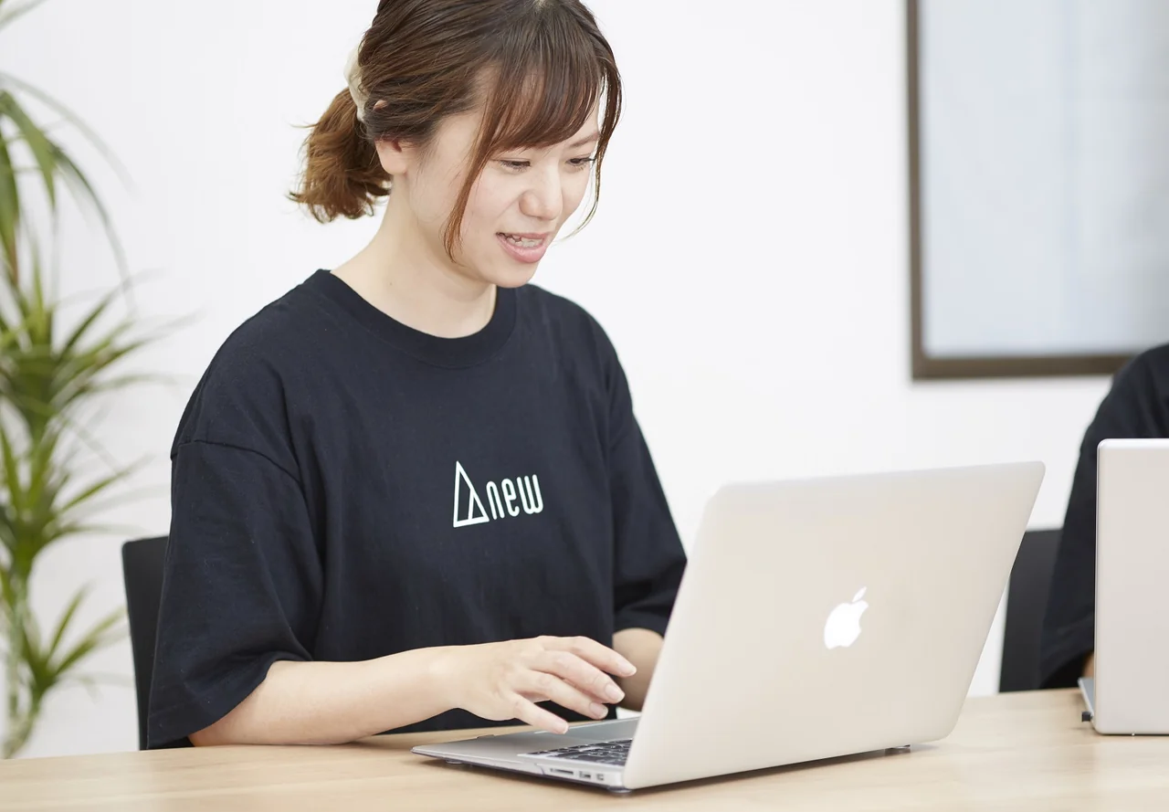 ANEWのロゴ入りTシャツを着てパソコンで作業するスタッフ